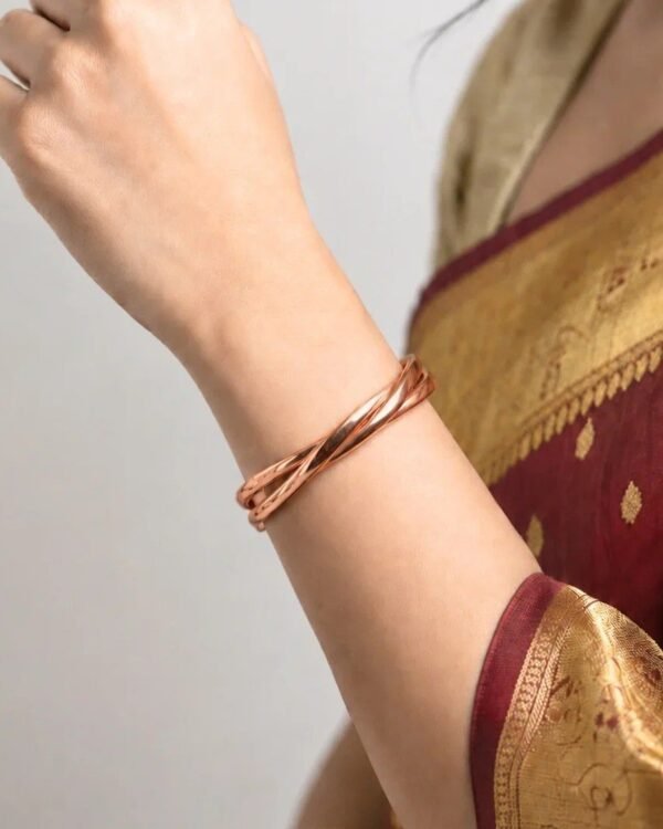 Woman wearing a twisted copper kada on her wrist with a red and gold saree