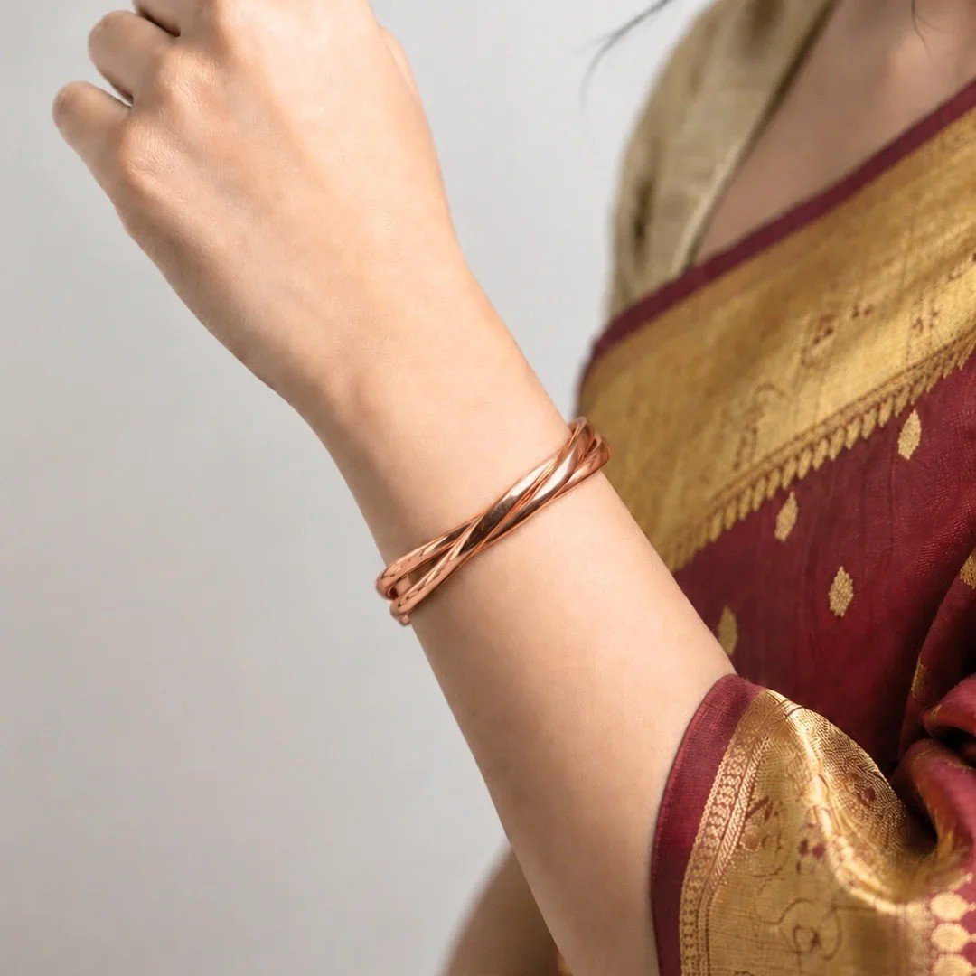 Woman wearing a twisted copper kada on her wrist with a red and gold saree