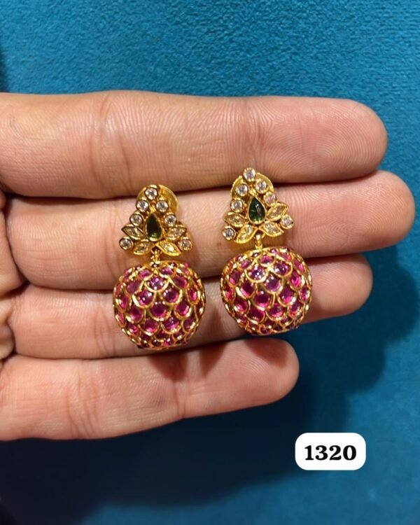 Pair of gold-tone jhumka earrings with pink stone domes held in a hand
