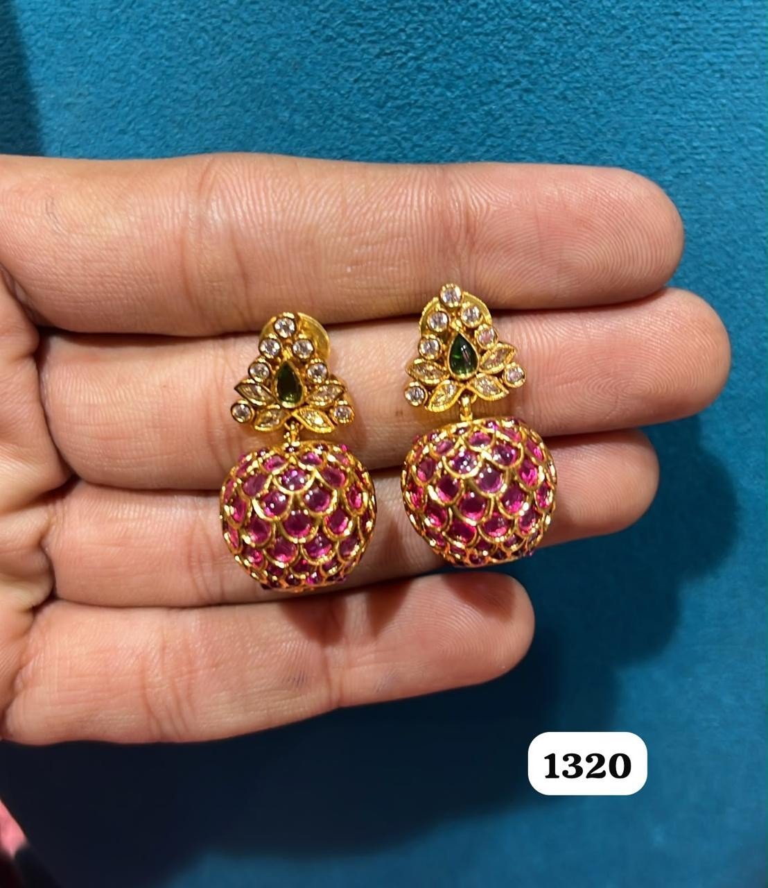 Pair of gold-tone jhumka earrings with pink stone domes held in a hand
